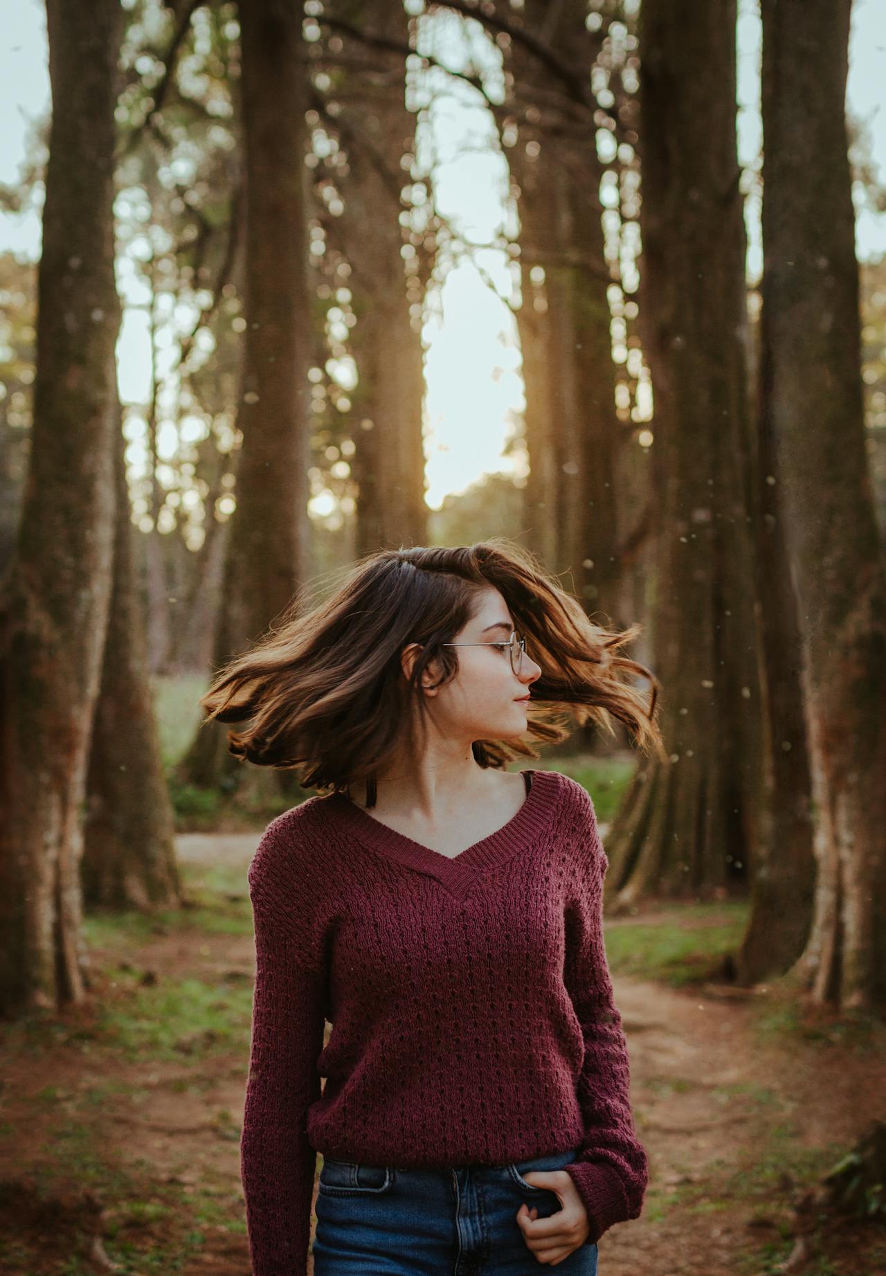 Young woman in a maroon sweater spinning around in a forest, with her hair in motion.