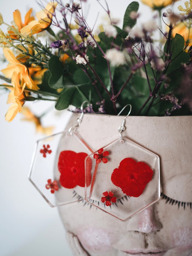 Hexagonal resin earring with pressed red flowers hanging on a flower pot.